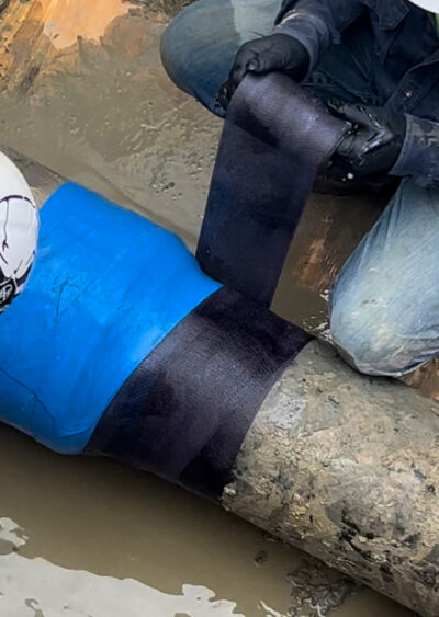 Picture of Pipe in ditch with ground water, protecting pipe with Blue Wrap known as VISCOTAQ and a Black Protective Layer outerwear known as FURS Composite knitted version